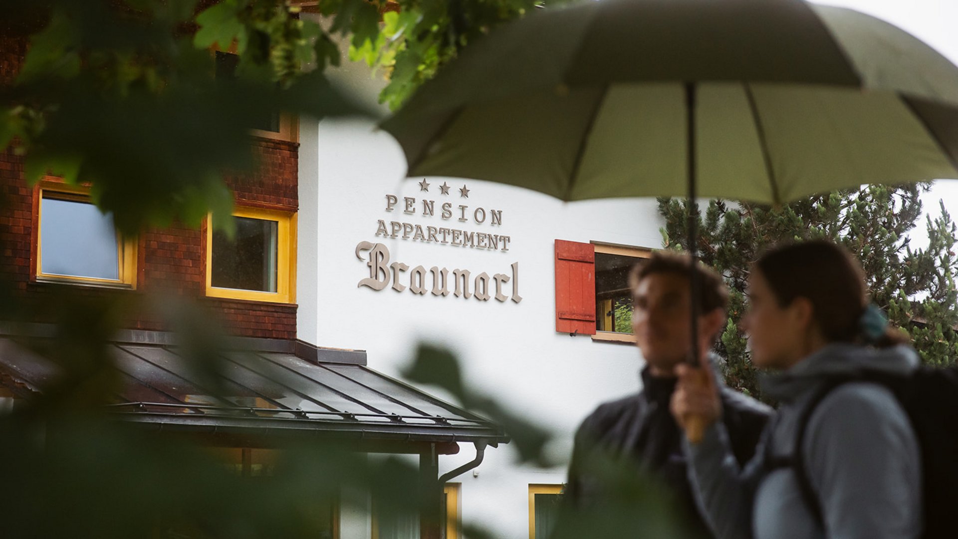 Ihre Ferienwohnung in Lech am Arlberg Pension Appartement Braunarl mit zwei Personen unter Regenschirm im Vordergrund