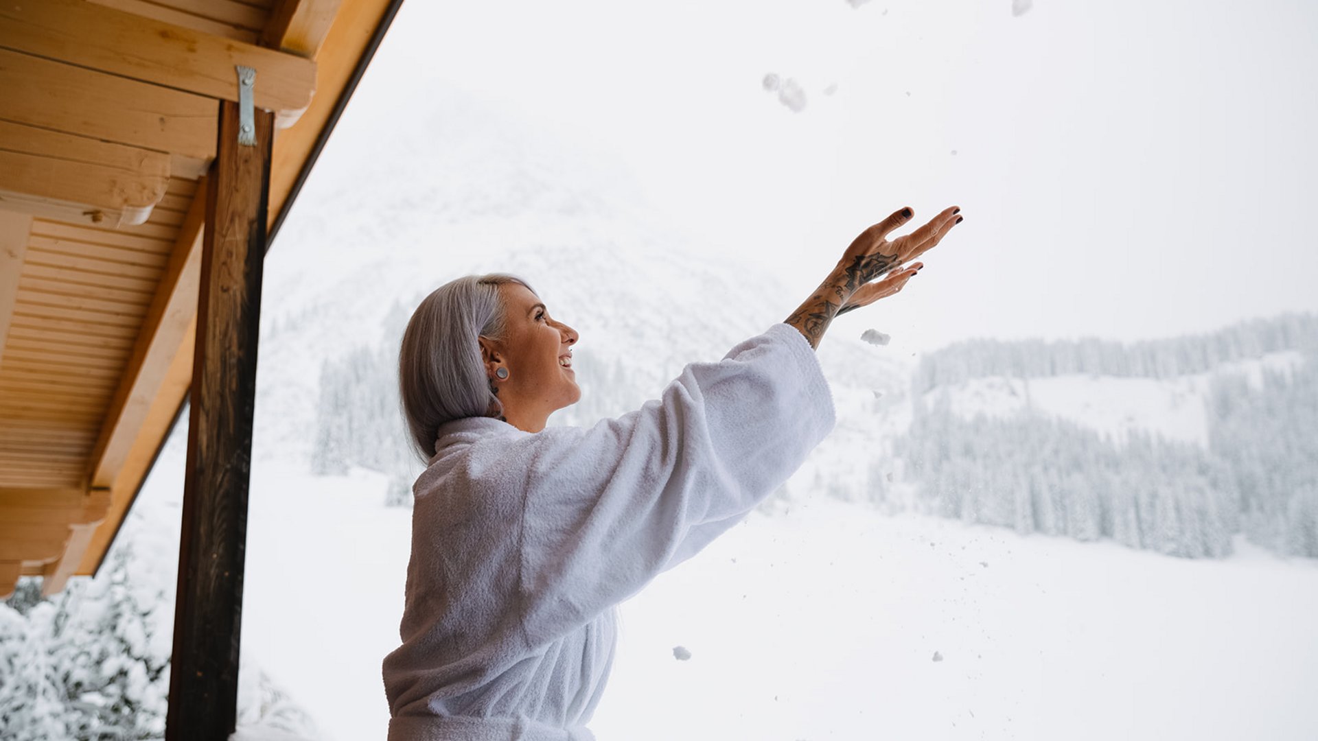 Ihre Ferienwohnung in Lech am Arlberg Frau im Bademantel spielt mit Schnee auf Balkon mit verschneitem Bergblick