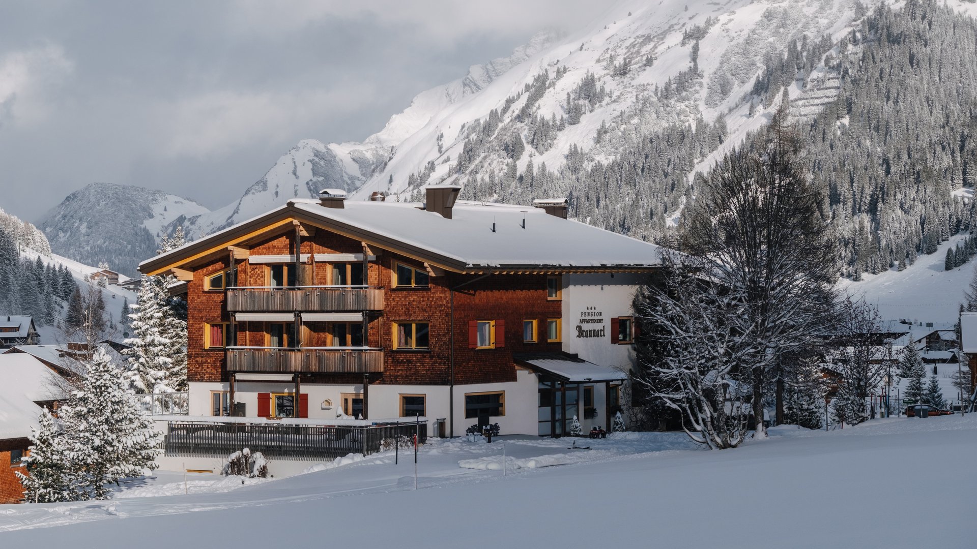 Ihre Ferienwohnung in Lech am Arlberg Hotelgebäude im verschneiten Alpenort vor bewaldeten Bergen